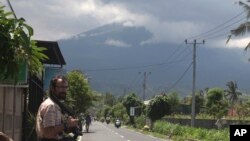 Mark Levitin, 39, a freelance photographer from Russi,a stands on a street with a backdrop of the Mount Agung volcano covered by cloud in Karangasem, Bali, Indonesia, Nov. 29, 2017. 