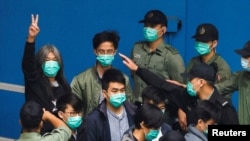 資料照：香港前立法會議員、民主活動人士梁國雄（左後做勝利手勢者 ）與其他活動人士一起走向一輛囚車，因受國家安全法指控而前往法庭。（ 2021年3月4日）