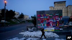 Un hombre camina junto a sacos de arena que forman la palabra "Ayuda" en la plaza Maidan en Kyiv, Ucrania, el 6 de junio de 2022. (Foto AP/Natacha Pisarenko)