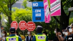 Protesters hold signs as police officers stand guard during a rally outside of the Foreign Ministry, where a trilateral meeting among the United States, South Korea and Japan was held in Seoul, South Korea, June 3, 2022. 