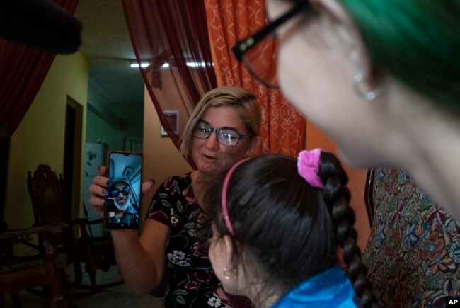 Danmara Triana holds her cell phone to show a live video image of her husband Roberto de la Iglesia, who has lived in the U.S. since 2015 with their son, during a video call with their daughters Alice and Claudia in Cienfuegos, Cuba, Thursday, May 19, 2022. (AP Photo/Ramon Espinosa)