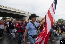 Seorang migran membawa bendera AS sambil membawa barang bawaannya meninggalkan kota Tapachula di negara bagian Chiapas, Meksiko, Senin pagi, 6 Juni 2022. (Foto AP/Isabel Mateos)