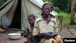 FILE - A refugee mother holds a ration card that allows her free supplies such as cooking oil, soap and sorghum as she sits with her young daughter outside their tent in Amboko camp, southern Chad. taken Sept. 3, 2005.