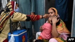 A health worker administers polio vaccine drops to a child during a door-to-door polio vaccination campaign at a slum area in Lahore, Pakistan, May 23, 2022. 