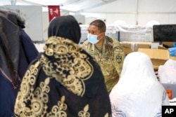 FILE - In this image provided by the U.S. Army, Army 1st Lt. Sanjay Gauntlette hands out essential items to U.S.-affiliated Afghans prior to their departure from Camp Liya, Kosovo, Oct. 16, 2021.