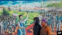 FILE - A couple wearing face masks walk past a painting to mark the country's Youth Day holiday in Soweto, South Africa, June 16, 2020. 