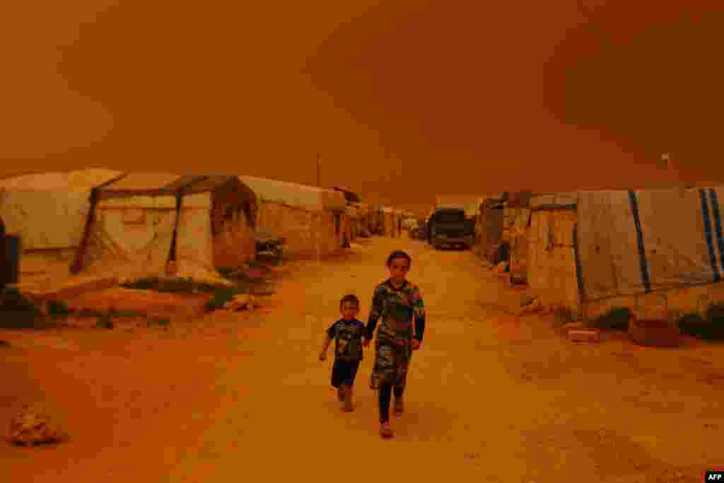 Displaced children walk past tents during a dust storm on the outskirts of the rebel-held town of Dana, in the northwestern Idlib province near the Turkish-Syrian border.