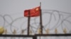 FILE - The Chinese flag flies behind razor wire at a housing compound in Yangisar, south of Kashgar, in China's western Xinjiang region, June 4, 2019.