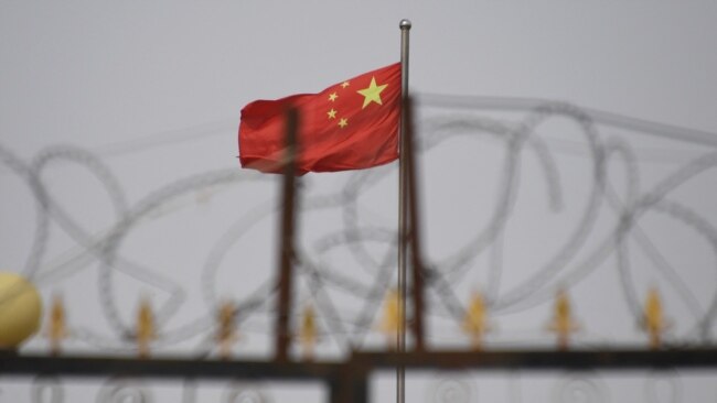 FILE - The Chinese flag flies behind razor wire at a housing compound in Yangisar, south of Kashgar, in China's western Xinjiang region, June 4, 2019.