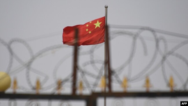 FILE - The Chinese flag flies behind razor wire at a housing compound in Yangisar, south of Kashgar, in China's western Xinjiang region, June 4, 2019.