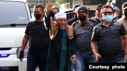 Pemimpin Khilafatul Muslimin, Abdul Qadir Hasan Baraja (tengah memakai sorban putih) didampingi para penyidik tiba di Polda Metro Jaya pada Selasa sore setelah dirinya ditangkap Selasa pagi di Teluk Betung, Bandar Lampung. (Foto: VOA/Indra Yoga)