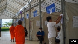 Buddhist monks walk pass a polling station as a man reviews a voter list ahead of commune election day, in Phnom Penh, on Saturday, June 4, 2022. (Khan Sokummono/VOA Khmer)