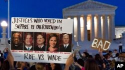 FILE - A demonstrator holds up a a sign with pictures of Supreme Court Justices Clarence Thomas, Brett Kavanaugh, Samuel Alito, Amy Coney Barrett, and Neil Gorsuch, as people protest outside of the U.S. Supreme Court, May 3, 2022.
