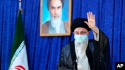 Supreme Leader Ayatollah Ali Khamenei waves to the crowd on the anniversary of the death of Ayatollah Khomeini, shown in the photo at top center, at his mausoleum in Tehran, Iran, June 4, 2022.