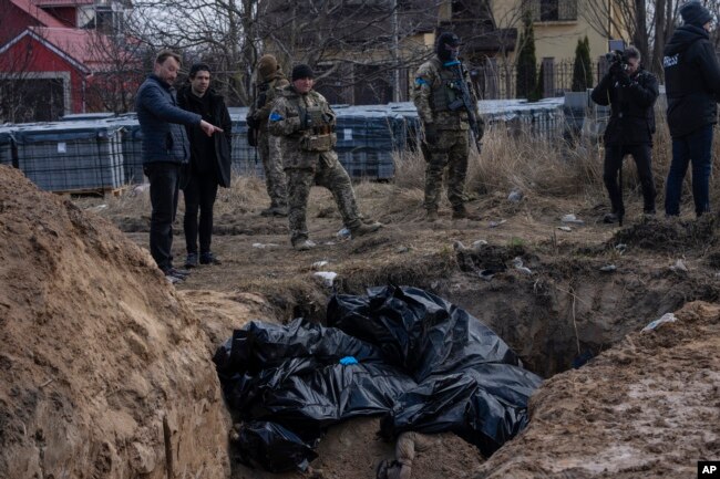 People stand next to a mass grave in Bucha, on the outskirts of Kyiv, Ukraine, Monday, April 4, 2022. (AP Photo/Rodrigo Abd)