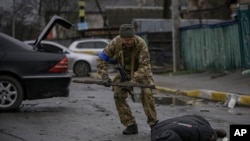 Një ushtarak ukrainas kontrollon kufomën e një civili në rast se është vendosur ndonjë kurth me eksploziv (Butcha, 2 prill 2022)