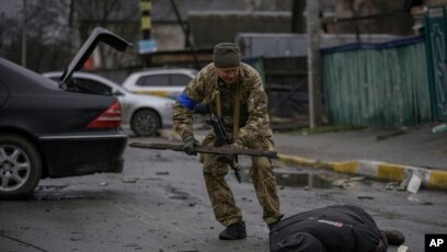 Një ushtarak ukrainas kontrollon kufomën e një civili në rast se është vendosur ndonjë kurth me eksploziv (Butcha, 2 prill 2022)