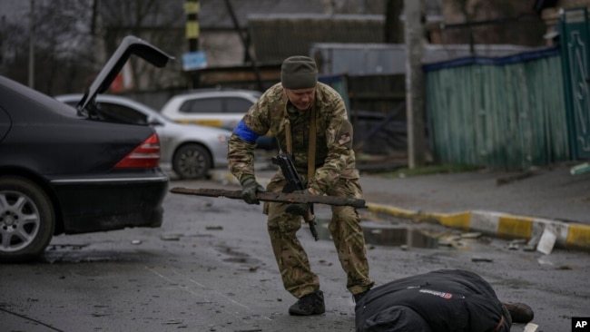 Një ushtarak ukrainas kontrollon kufomën e një civili në rast se është vendosur ndonjë kurth me eksploziv (Butcha, 2 prill 2022)