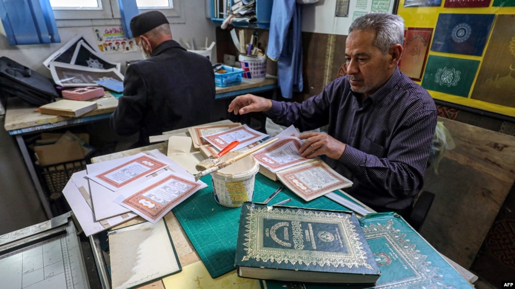 Libyan restorer of the Holy Koran Khaled al-Drebi (R), assembles pages together to be glued into a volume during a workshop on the restoration of copies of Islam's holy book, in Libya's capital Tripoli on March 22, 2022. (Photo by Mahmud Turkia / AFP)