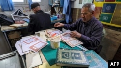 Khaled al-Drebi (kanan) tampak menyusun halaman-halaman Al-Quran untuk direkatkan kembali menjadi satu dalam pelatihan perbaikan Al-Quran lama di Tripoli, Libya, pada 22 Maret 2022. (Foto: AFP/Mahmud Turkia)