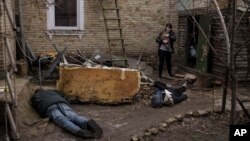 A woman holds her cat as she walks next to the bodies of her husband, brother, and another man, who were killed outside her home in Bucha, on the outskirts of Kyiv, Ukraine, April 4, 2022.
