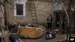 Ira Gavriluk holds her cat as she walks next to the bodies of her husband, brother, and another man, who were killed outside her home in Bucha, on the outskirts of Kyiv, Ukraine, April 4, 2022.