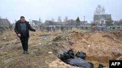 FILE - A man gestures at a mass grave in the town of Bucha, northwest of the Ukrainian capital, Kyiv, on Apr. 3, 2022.