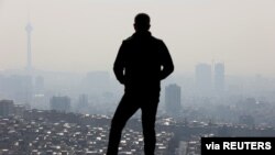 FILE - A man stands in front of a general view of Tehran city following the increase in air pollution in Tehran, Iran, Nov. 24, 2021. 