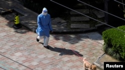 A person in personal protective equipment (PPE) walks a dog at a resident community, as the second stage of a two-stage lockdown has been launched to curb the spread of the coronavirus disease (COVID-19) in Shanghai, China April 3, 2022. 