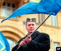 FILE - Wearing a Serbian army cap, Russian nationalist leader Vladimir Zhirinovsky, waves his party flag demanding an end to NATO attacks on Yugoslavia outside the U.S. Embassy in Moscow, March 25, 1999.