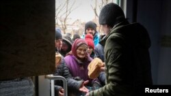 Warga lokal di Mariupol menerima bantuan berupa roti pada 4 April 2022. Pemberian bantuan dilakukan di tengah konflik antara Rusia dan Ukraina di mana pasukan Rusia masih menguasai kota pelabuhan tersebut. (Foto: Reuters/Chingis Kondarov)