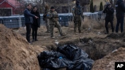 FILE - People stand next to a mass grave in Bucha on the outskirts of Kyiv, Ukraine, April 4, 2022.