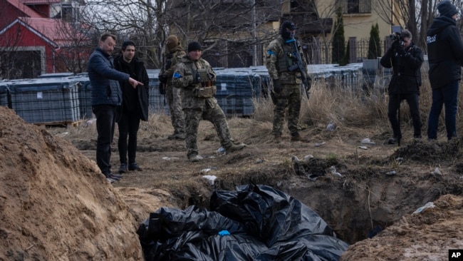 ARCHIVO - Personas junto a una fosa común en Bucha, en las afueras de Kiev, Ucrania, el 4 de abril de 2022. Periodistas de AP vieron decenas de cuerpos en Bucha, muchos de ellos disparados a quemarropa y algunos con las manos atadas a la espalda. . (Foto AP/Rodrigo Abd, Archivo)