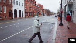 Seorang perempuan menyeberang jalan yang di Georgetown, di Washington DC yang tampak sepi. Biasanya, kawasan perbelanjaan itu ramai pengunjung, 23 Maret 2020. (Foto: AFP)