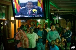 ປະຊາຊົນຊິມບັບເວ ກຳລັງເບິ່ງໂທລະພາບ ຖະແຫລງການຂອງ ປະທານາທິບໍດີ Robert Mugabe ຢູ່ທີ່ບາດື່ມເຫລົ້າໃນເມືອງ Harare ປະເທດ Zimbabwe.