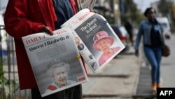 Pedestrians walk past a vendor selling local dailies carrying the headlines reporting the news of the death of Queen Elizabeth II, in Nairobi on Sept. 9, 2022.