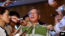 FILE - Okinawa Gov. Takeshi Onaga, center, speaks to the media after meeting with Japanese Prime Minister Shinzo Abe at Abe's office in Tokyo.