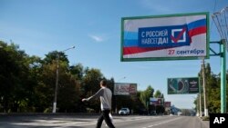 Un hombre cruza una calle el jueves 22 de septiembre de 2022 junto a un letrero que dice: "Con Rusia para siempre, 27 de septiembre" antes de un referendo en Luhansk, en la República Popular de Luhansk _controlada por separatistas prorrusos_, en el este de Ucrania. (AP Foto)