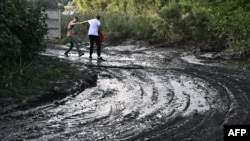 FILE: This photograph, taken Sept. 16, 2022, shows two pedestrians crossing a mud-covered road in the town of Kryvyi Rih, where dozens of homes were flooded after a Russian attack damaged a dam upstream on Sept. 14, 2022.
