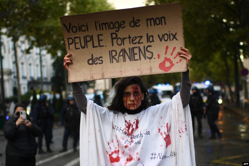 A protestor holds a banner reading "This is the image of my people. Carry the voice of the Iranians" as she stands in front of riot police during a demonstration in support of Iranian protesters in Paris, on Sept. 25, 2022.