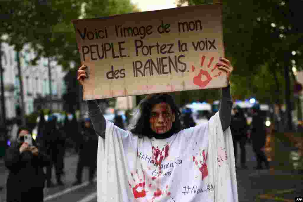 A protestor holds a banner reading &quot;This is the image of my people. Carry the voice of the Iranians&quot; as she stands in front of riot police during a demonstration in support of Iranian protesters in Paris, on Sept. 25, 2022.