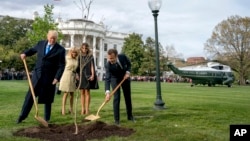 FILE - U.S. President Donald Trump, left, and French President Emmanuel Macron participate in a tree planting ceremony on the South Lawn of the White House in Washington on April 23, 2018. Also in the photo are Brigitte Macron, second left, and Melania Trump.