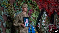 Seorang tentara Ukraina memegang foto Olga Simonova, perempuan Rusia yang tewas membela Ukraina dalam pertempuran melawan Rusia di wilayah Donetsk, Kyiv, Ukraina, Sabtu, 16 September 2022. (Foto: AP Photo/Roman Hrytsyna)