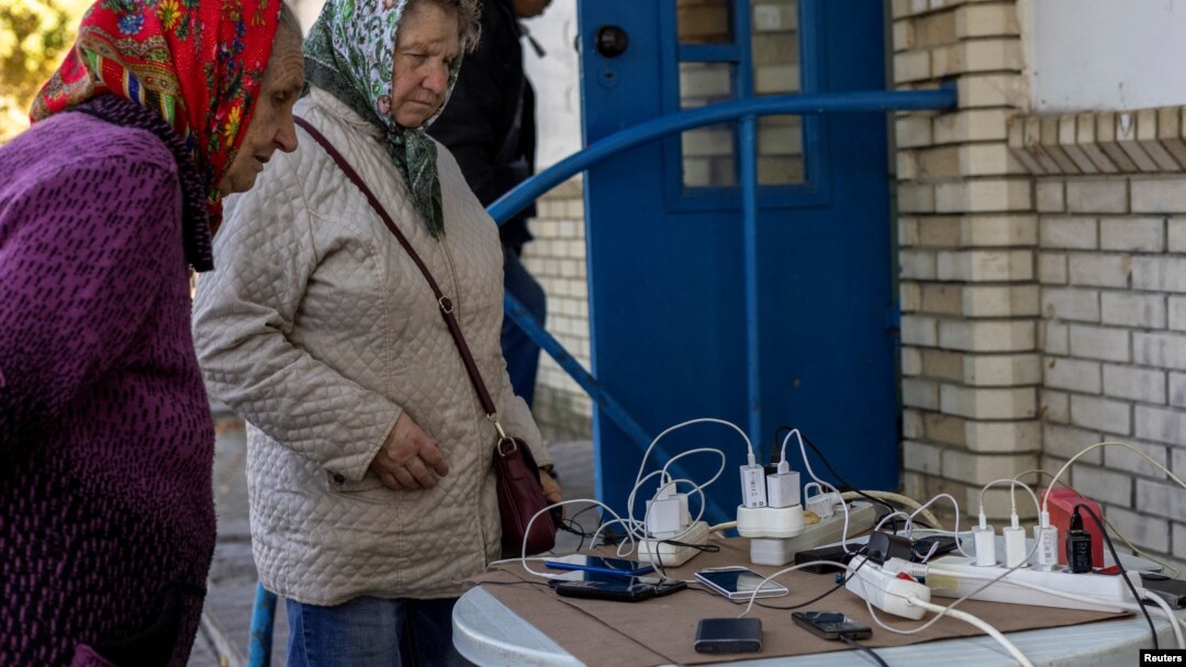 Locals charge their mobile phones with the electricity provided from a generator in front of a shop as there is no electricity in Balakliia, recently liberated by Ukrainian Armed Forces, in Kharkiv region, Sept. 21, 2022. 
