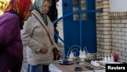 Locals charge their mobile phones with the electricity provided from a generator in front of a shop as there is no electricity in Balakliia, recently liberated by Ukrainian Armed Forces, in Kharkiv region, Sept. 21, 2022. 