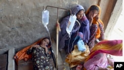 2022年9月15日，在巴基斯坦俾路支省贾法拉巴德，一名患病的女孩和妇女在一座废弃建筑内搭建的临时医疗中心接受治疗。