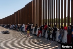 FILE - Asylum-seeking migrants, mostly from Venezuela and Cuba, wait to be transported by U.S. Customs and Border Protection agents after crossing the Rio Grande River into the U.S. from Mexico at Eagle Pass, Texas, July 14, 2022.