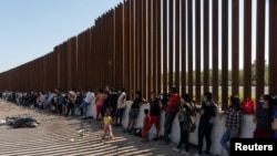 Sejumlah migran pencari suaka, yang kebanyakan berasal dari Venezuela dan Kuba, menunggu untuk dipindahkan oleh petugas Perbatasan dan Bea Cukai AS di area perbatasan AS-Meksiko di Eagle Pass, Texas, pada 14 Juli 2022. (Foto: Reuters/Go Nakamura)