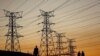 FILE - Locals walk past electricity pylons during frequent power outages from South African utility Eskom, caused by its aging coal-fired plants, in Soweto, South Africa, July 3, 2022.