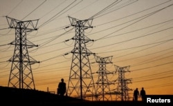 FILE - Locals walk past electricity pylons during frequent power outages from South African utility Eskom, caused by its aging coal-fired plants, in Soweto, South Africa, July 3, 2022.